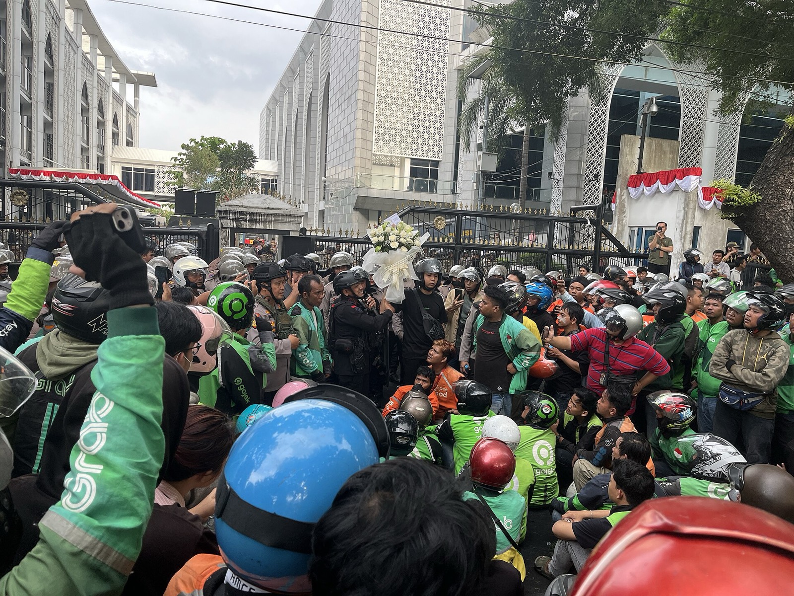 Kerumunan pengunjuk rasa berhelm dan berjaket hijau di depan sebuah gedung di Medan