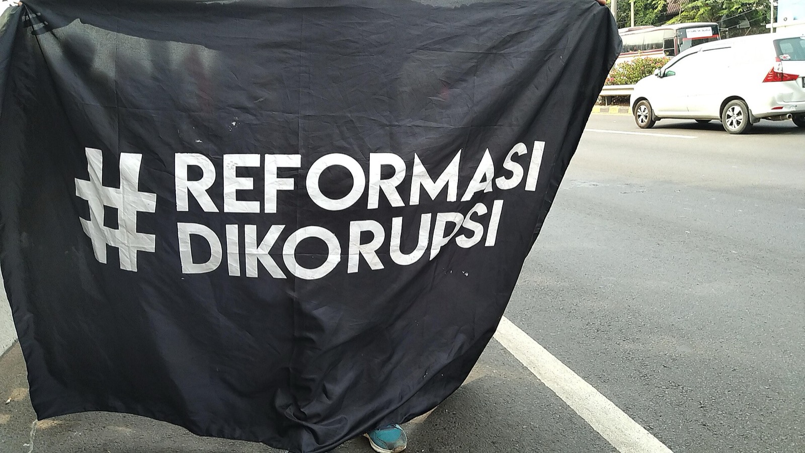 Spanduk hitam bertuliskan #ReformasiDikorupsi dibentangkan di jalan saat unjuk rasa di Jakarta